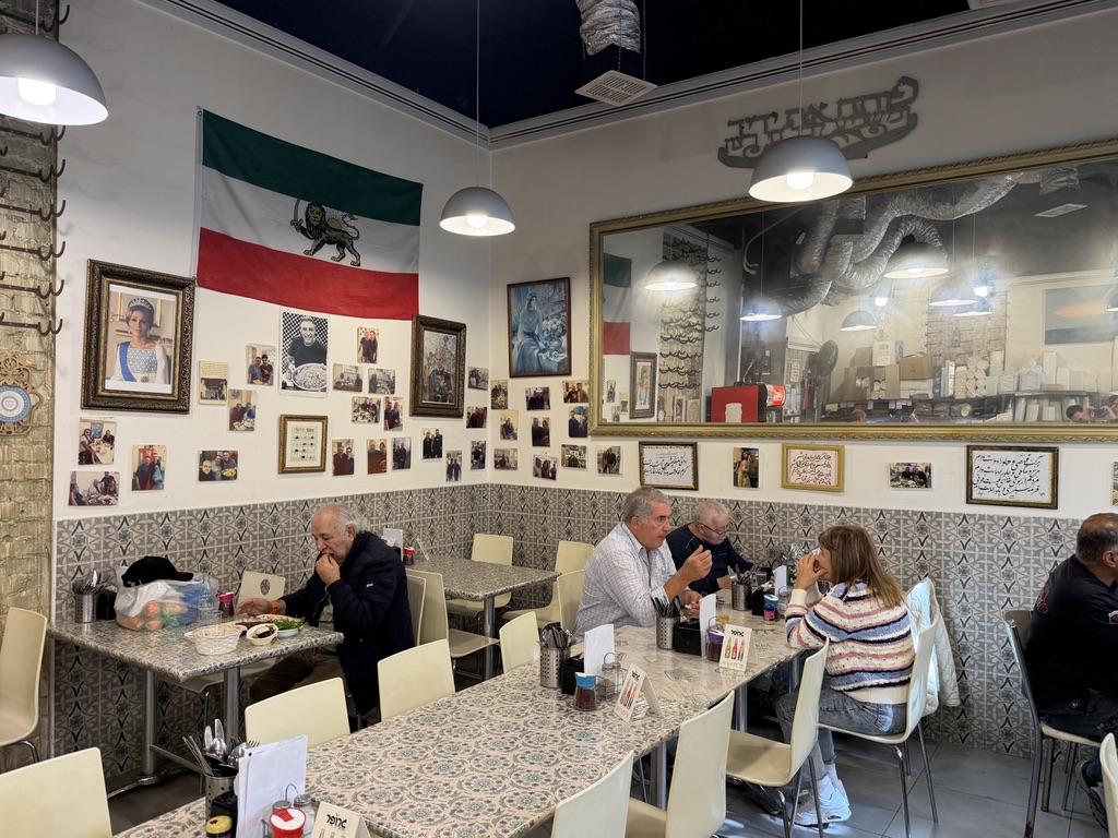 Interior of Gourmet Sabzi restaurant in Levinsky Market Tel Aviv with framed photos of Shah Mohammad Reza Pahlavi and Empress Farah on the wall beside the pre-revolution Iranian flag.