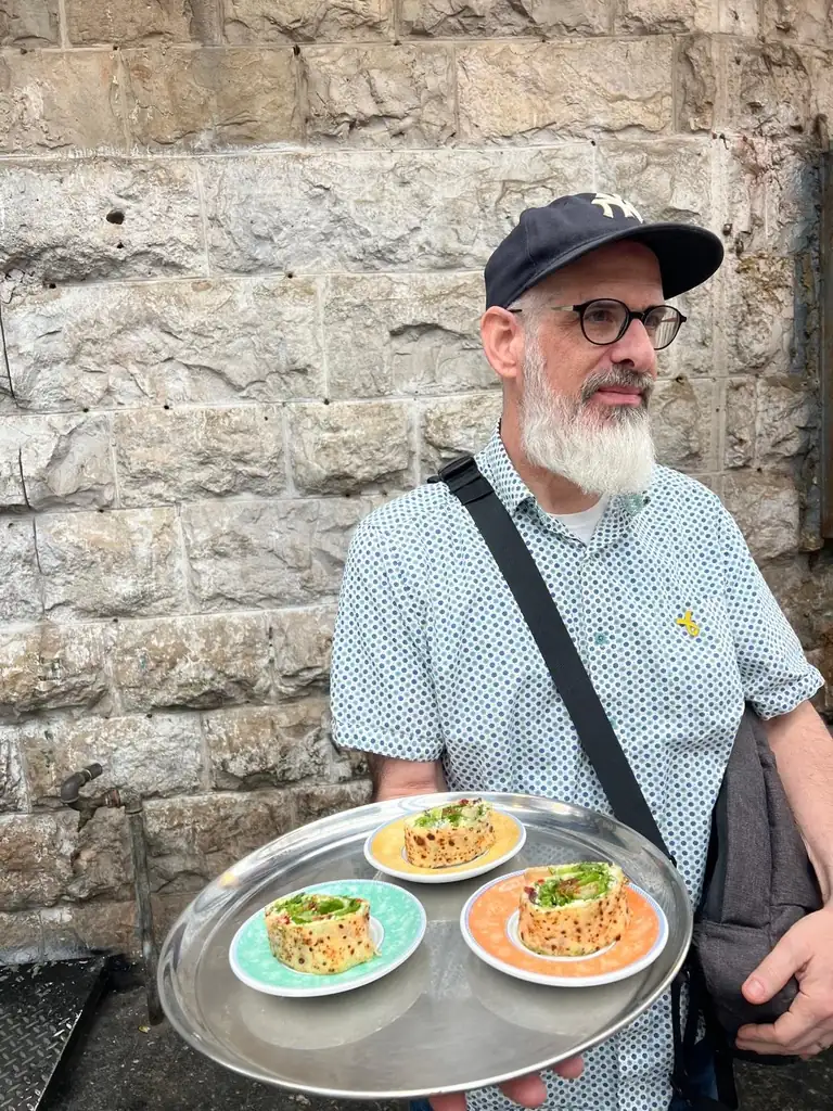 Harry Rubenstein standing at Nona Mufletta in Mahane Yehuda Market, Jerusalem, holding a freshly made mufletta.